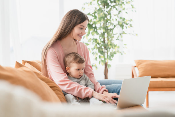 年轻的单身忙碌的母亲带着蹒跚学步的儿子和刚出生的婴儿在产假期间使用笔记本电脑远程工作。在隔离期间做自由职业在线学习和儿童购物图片下载