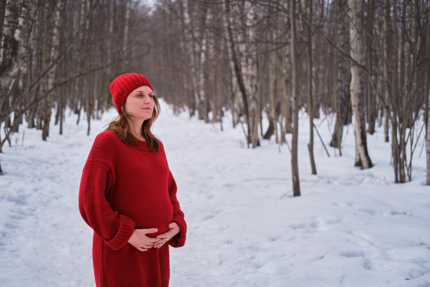 一位身穿针织毛衣、头戴帽子的快乐孕妇在公园里散步图片下载