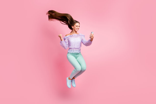 幸运少女全身照片穿着休闲装手持现代设备上升拳头孤立的淡粉色颜色背景图片下载