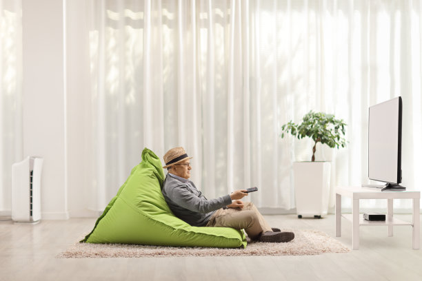 一个拿着遥控器的老人坐在沙发上看电视图片下载