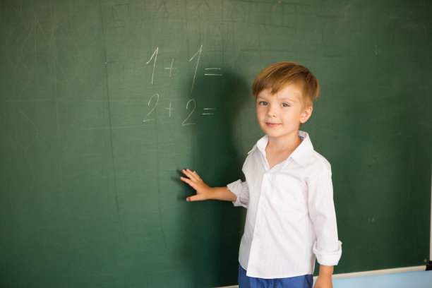 一个可爱的小男孩在学校站在黑板旁边写字。回到学校的概念图片下载