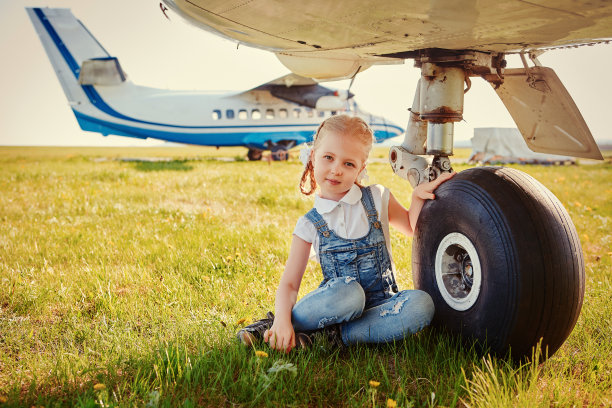 可爱的小女孩坐在飞机起落架旁边，梦想着在飞机上旅行和飞行图片下载