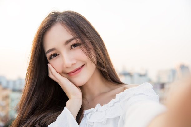 年轻美丽的亚洲女人的肖像放松使用智能手机自拍生活在天空屋顶。微笑快乐的亚洲女孩网红博主。教育电子商务技术连接人们的生活方式理念图片下载