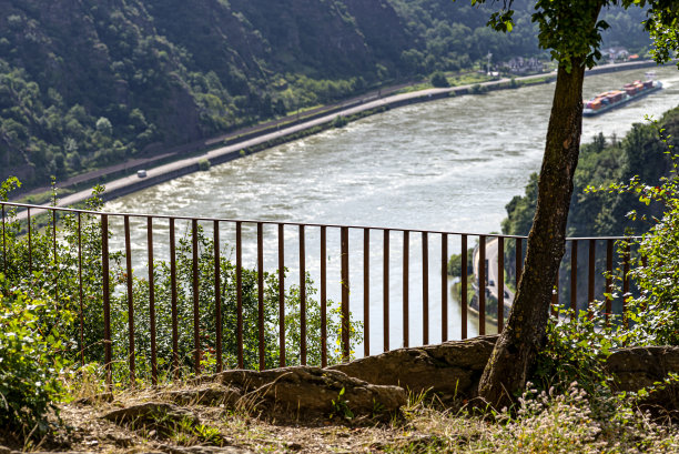 河谷边缘有生锈的金属栅栏，山上和河边有可见的树木。图片下载