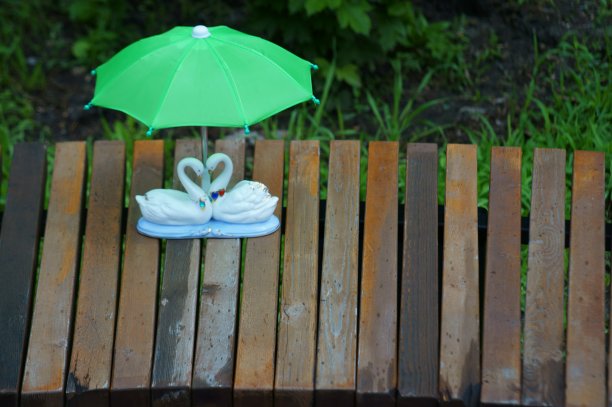 一对在玩具伞下相爱的天鹅雕像。图片下载
