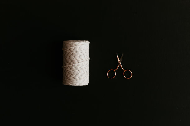 一卷白棉绳，一把黑色背景上的玫瑰金剪刀。图片下载