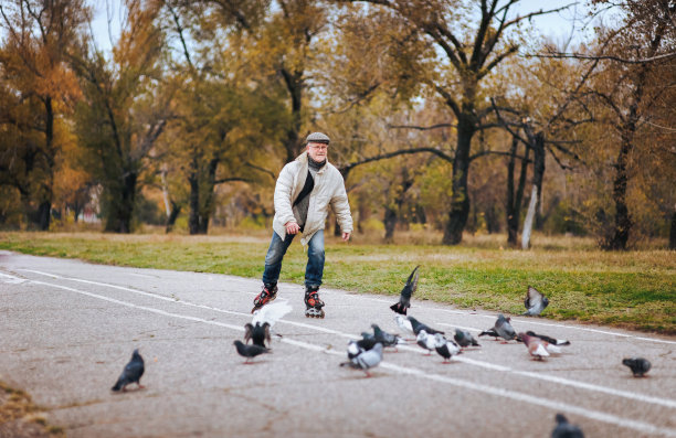 一位上了年纪的人喜欢穿旱冰鞋溜冰。活跃的老人。那人张开双手。人们和鸽子。快乐的养老金。活跃的老人。图片下载