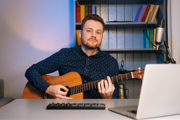 年轻的吉他手在录音室里一边弹吉他一边对着麦克风唱歌，看着摄像机。图片下载
