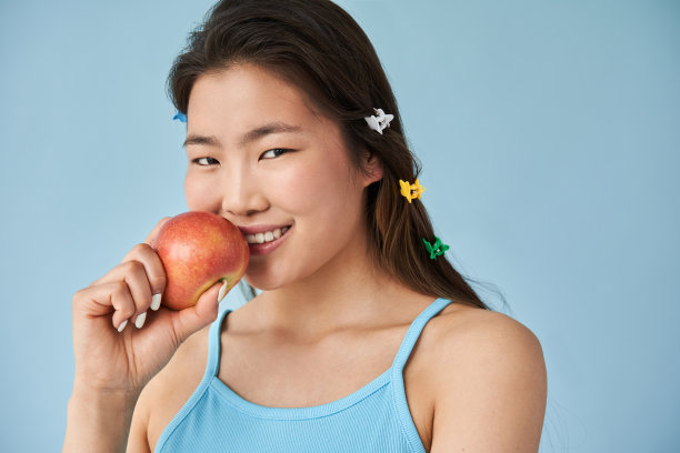 在摄影棚拍摄时，一个女人拿着苹果看着相机图片下载