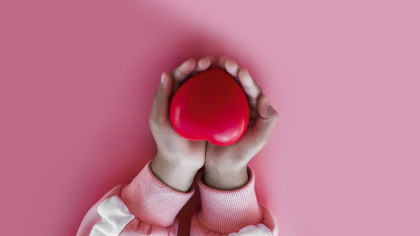 小女孩手拿红心在粉红色的背景。图片下载