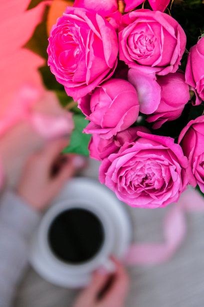 一杯咖啡和粉红色的玫瑰。节日概念，生日时送一束玫瑰，早餐时送一束鲜花。女人的手拿着卡布奇诺图片下载