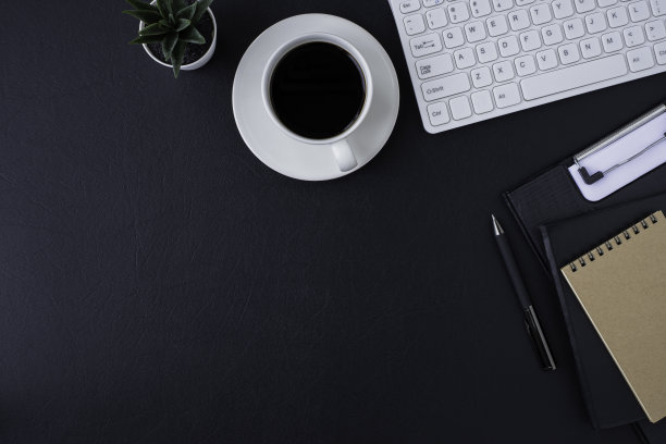 黑色皮革办公桌椅。工作空间有电脑、白色键盘和空白笔记本、笔和设备等办公用品。图片下载