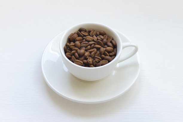 桌上有个白色的马克杯，里面装着咖啡豆。图片下载