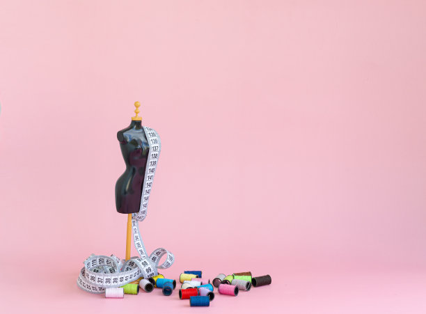 粉红色背景上的缩小模型，带着测量用的卷尺和线轴上五颜六色的线。图片下载