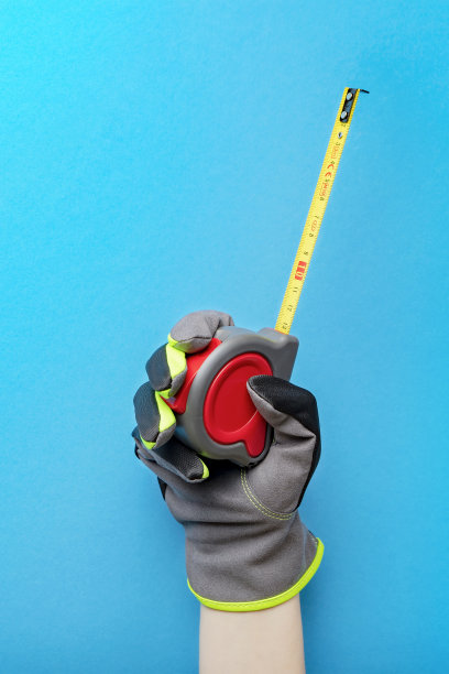 卷尺。拿着卷尺在蓝色背景上。修理和安装工具。垂直照片用于建筑主题的设计和印刷。图片下载