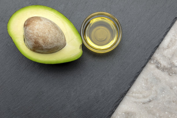 鳄梨油。石盘上放着一个带骨头的鳄梨。把鳄梨油倒进盘子里。横幅印刷，标签设计，健康食品。图片下载