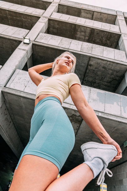 史诗般的低角度英雄照片，一个年轻，积极，健康的金发白种人女人站着，伸展她的四头肌，以恢复或准备户外跑步图片下载