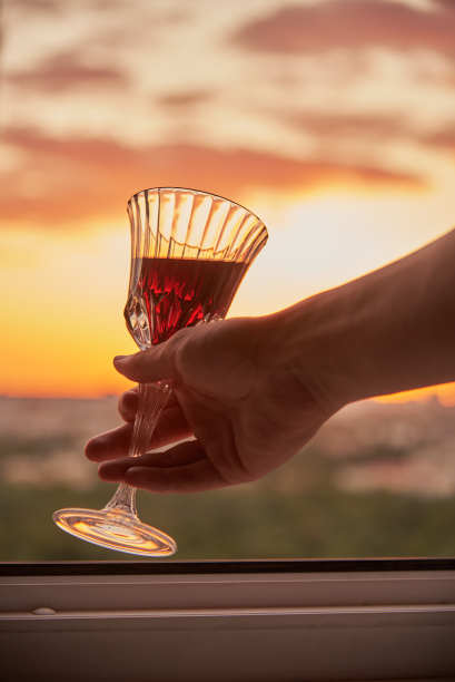 一个男人的手拿着一杯酒，背景是明亮的日落。图片下载