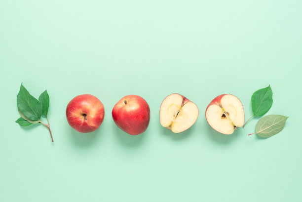 一整只红苹果和半只带叶子的苹果在绿色蜡笔纸上排成一排。俯视图，平铺，复制空间。图片下载