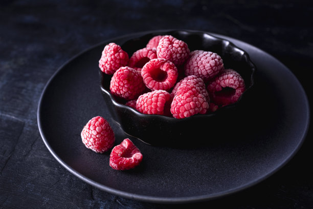 碗里的覆盆子和深色背景。冷冻水果。冰冻覆盆子的穆迪照片图片下载