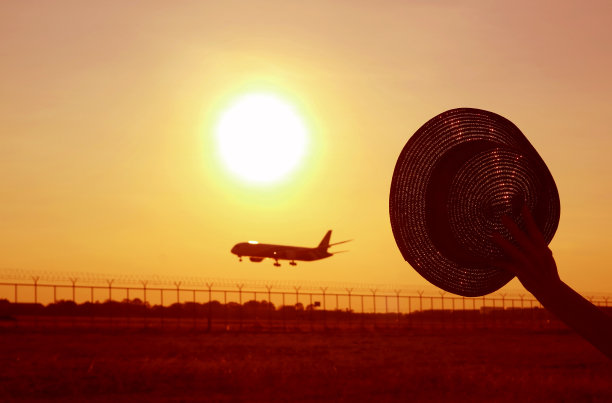 手拿帽子的剪影向飞机挥手，飞机飞上了日出的天空图片下载