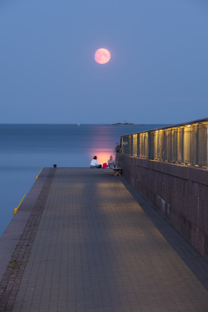 三个心不在焉的女人坐在码头的尽头，背景是满月。图片下载