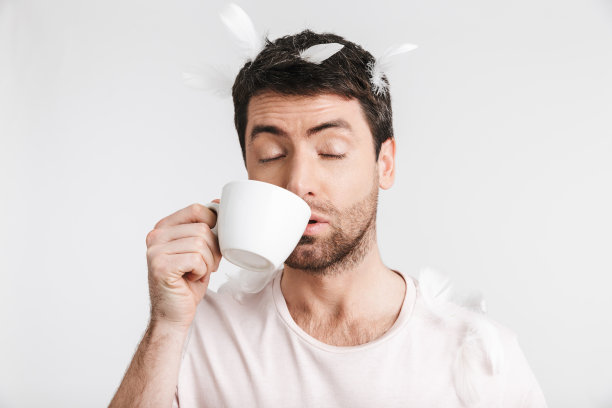 有魅力的30多岁男子穿着休闲t恤，站在飘落的羽毛下喝咖啡图片下载