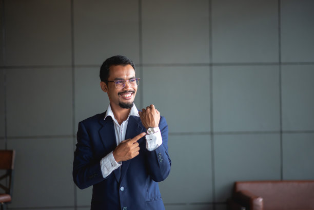 年轻英俊的商人戴着眼镜，坐在办公室的沙发上用触控板工作。图片下载