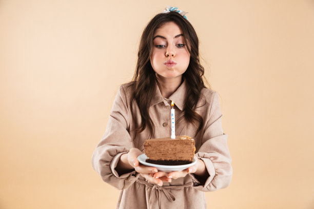 兴奋的年轻漂亮的女人在米色背景墙上抱着节日蛋糕。图片下载