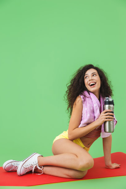 健康女孩的形象，20多岁，穿着运动服，脖子上围着毛巾，锻炼后坐在健身垫上休息图片下载