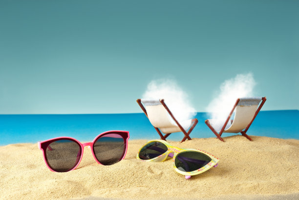 细细的沙子上粉红色的眼镜。沙滩椅背景上的眼镜。沙滩椅以蓝色的海水和天空为背景。白云在沙滩上晒日光浴。图片下载