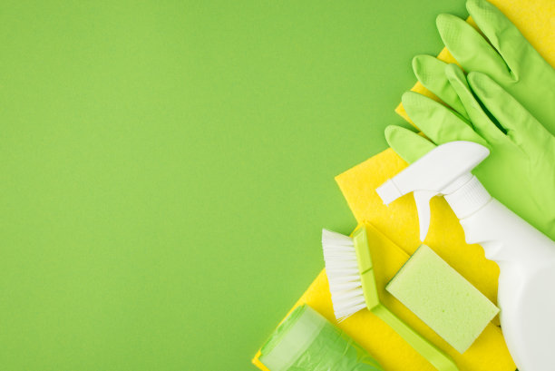 顶部视图照片的喷雾洗涤剂瓶子没有标签刷海绵黄色粘胶餐巾，垃圾袋和橡胶手套孤立的绿色背景与copyspace图片下载