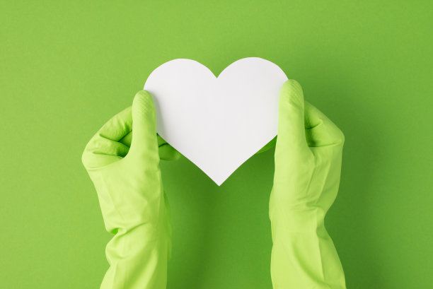俯视图照片双手在绿色橡胶手套手持白纸心与孤立的绿色背景空白图片下载