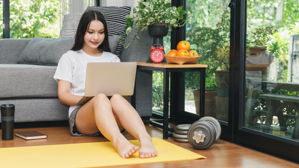 漂亮的年轻女子坐在客厅的地板上，在笔记本电脑上观看在线健身视频教程。图片下载