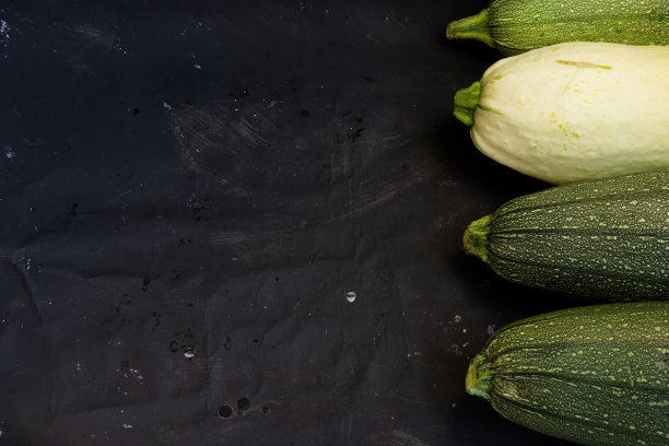 整个成熟的西葫芦放在时尚的黑色背景上，一张诱人的餐厅照片，一份素食菜单，平面上有广告空间。图片下载