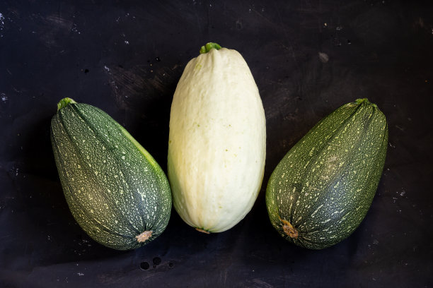 整个成熟的西葫芦放在时尚的黑色背景上，一张诱人的餐厅照片，一份素食菜单，平面上有广告空间。图片下载