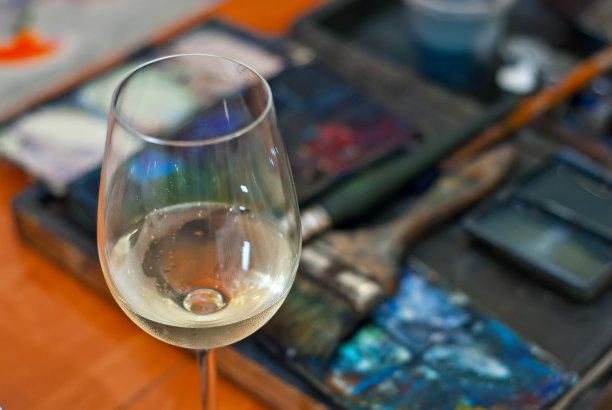 来杯白葡萄酒。调色板背景上的葡萄酒和颜料。创造力和灵感的概念。图片下载