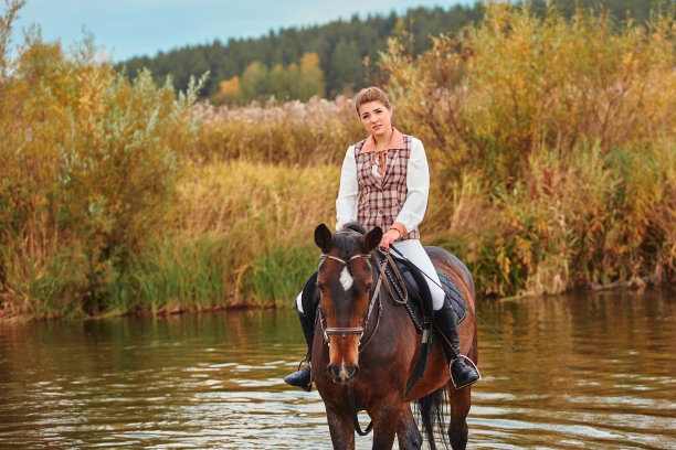 一个漂亮的女孩穿着骑手的运动服正骑在马上，他们走进了水库的水里图片下载