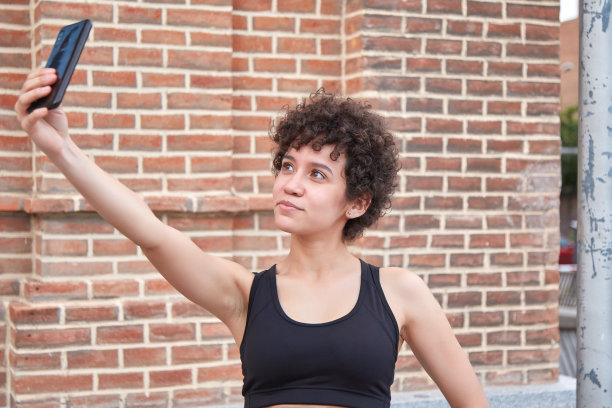 年轻的拉丁卷发在夏日的户外自拍。多米尼加女孩用手机自拍。图片下载