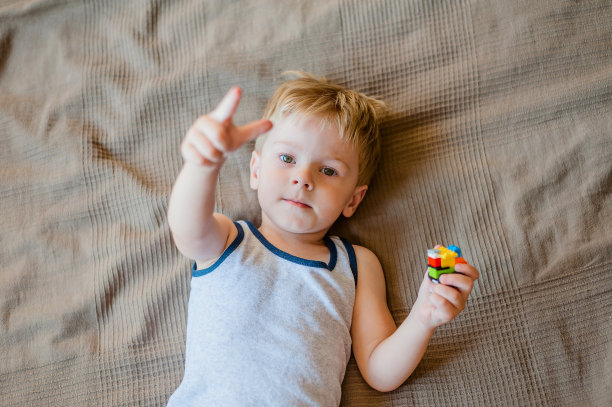 一个小男孩躺在床上，手里拿着一个塑料构造器，露出他的手指图片下载