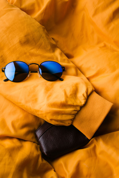 一套时尚的服装和配饰，红色运动鞋和蓝色太阳镜上的黄色夹克作为背景。图片下载
