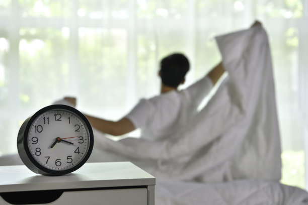 男人早上醒来时坐在床上伸伸懒腰，专注于闹钟图片下载