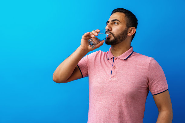 英俊的西班牙男子在蓝色背景下喝着一杯淡水图片下载