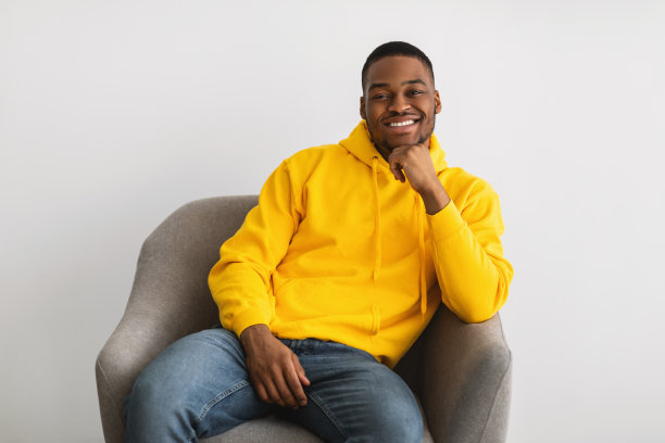 一个黑人坐在扶手椅上，在灰色背景下摆姿势图片下载