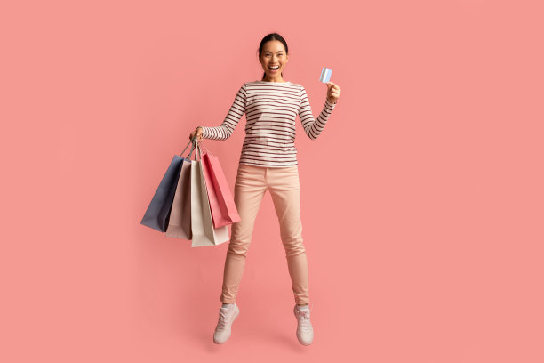 大的销售。兴奋的亚洲女性跳跃购物袋和信用卡图片下载