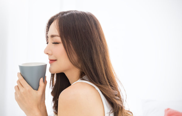 在白色的卧室里，年轻美丽的亚洲女人手握咖啡杯的早春时光。在夏天快乐愉快放松。韩国化妆大学生活理念。图片下载