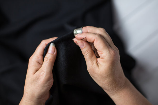 裁缝的手里。女手有针、线和顶针。女人缝深色衣服。Сonceptual想法。图片下载