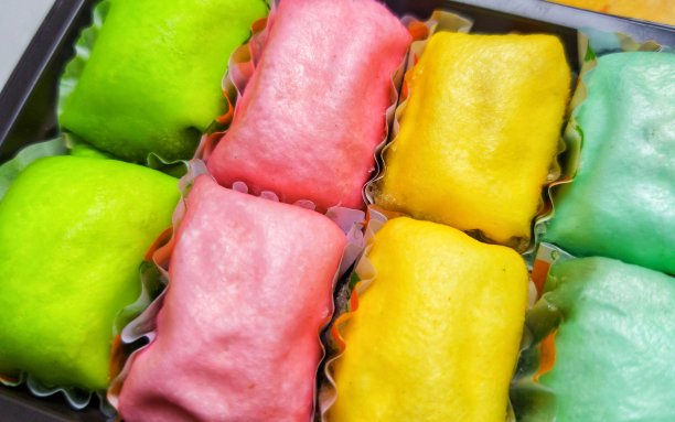 木桌上摆着一排排五颜六色的榴莲煎饼或榴莲薄饼，装在黑色的塑料盒子里图片下载