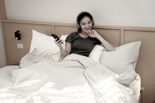 年轻的亚洲女性躺在床上用耳机听音乐或用手机看社交媒体网络休息放松时间图片下载
