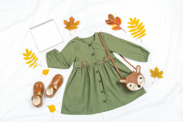 时尚的秋季套儿童衣服。绿色的衣服，棕色的包，鞋子，空白的笔记本模型和秋天的叶子在白色的背景。时尚女孩lookbook概念。模型俯视图平铺图片下载